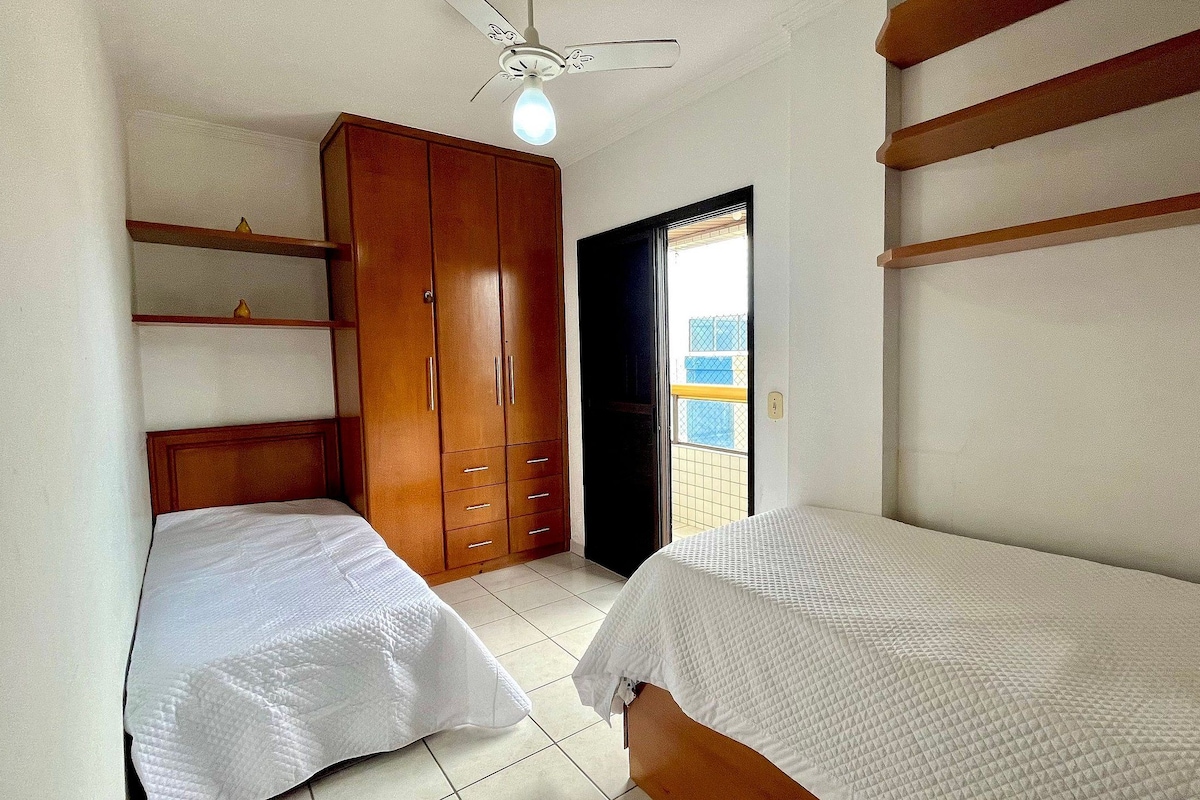 A bedroom with two single beds, a wooden wardrobe, a ceiling fan, and a balcony with a view.