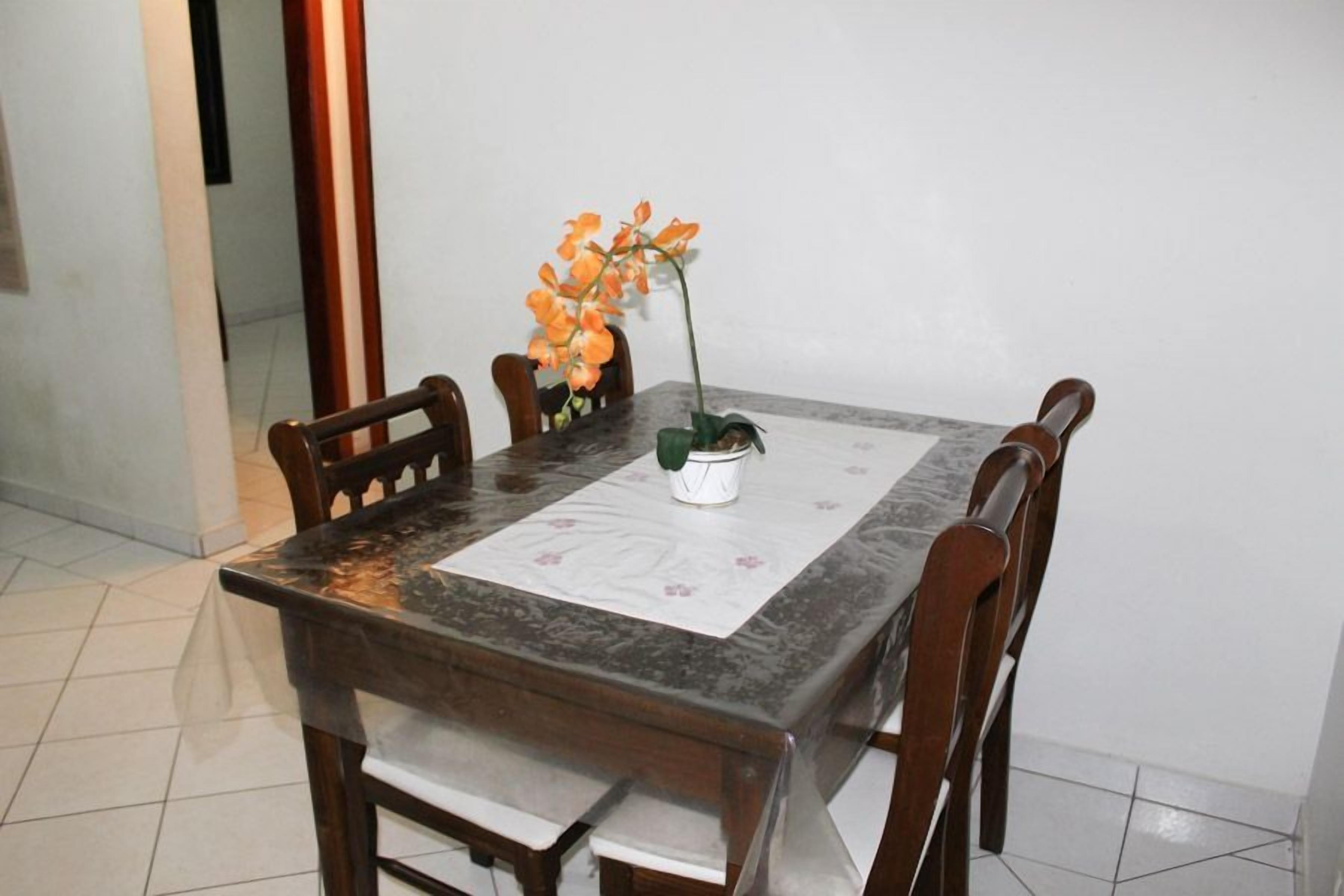 A dining table with a marble top, surrounded by wooden chairs, and a potted orchid on the table.