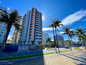 A tall residential building with multiple balconies, a paved road, and palm trees.
