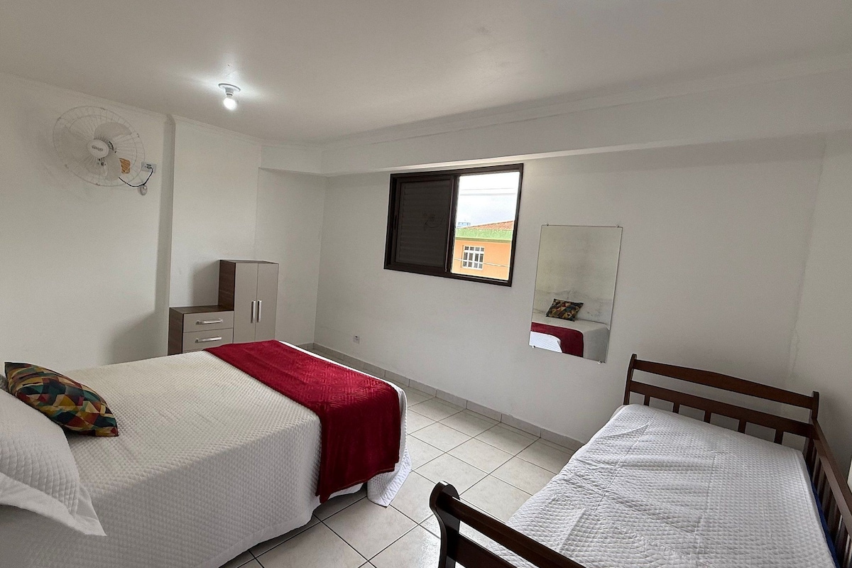 A bedroom with two beds, a wardrobe, a window, and a ceiling fan.