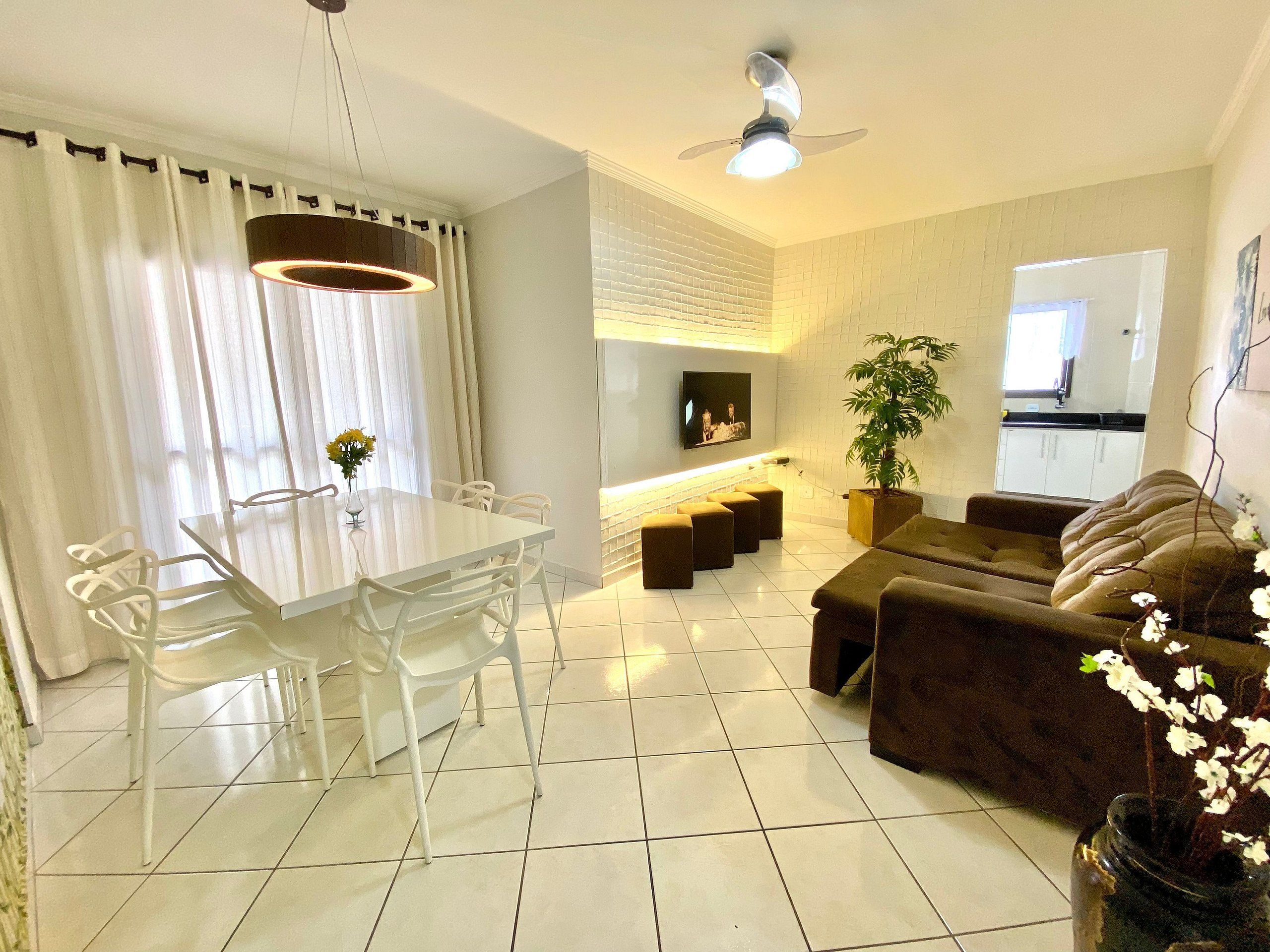 A modern living room with a dining area, a ceiling fan, a flat-screen TV, and a potted plant.