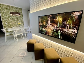 A modern dining area with a large flat-screen TV, white furniture, and a bamboo-patterned wall.