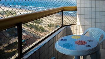 A balcony with a view of the beach, a tiled wall, and a round table with chairs.