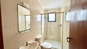 A bathroom with a toilet, sink, mirror, and glass shower enclosure.