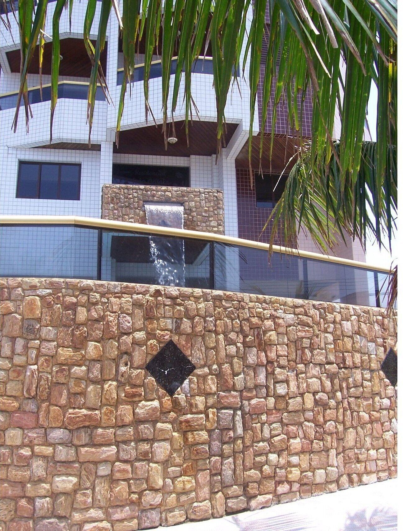 A stone wall with a water feature, a glass railing, and a building with windows in the background.
