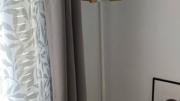 A white floor lamp with a modern design, positioned in a corner of a room with a wooden floor and a white wall.