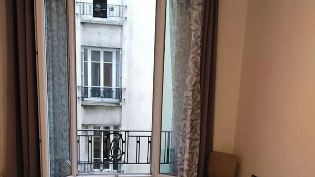 A bedroom with a bed, a radiator, a chair, and a window with curtains. - joseph appartment  (Paris)