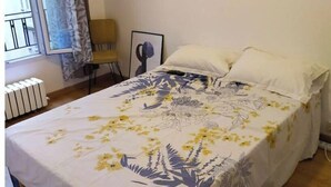 A bedroom with a bed, a window with curtains, a radiator, and a framed picture on the wall. - joseph appartment  (Paris)