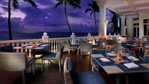 A restaurant with outdoor seating overlooking the ocean, featuring wicker chairs and tables set with dinnerware. - BEAUTIFUL Resort Located Directly On The Sand! - City View Room  (Fort Lauderdale)