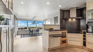 Eine moderne Küche mit Holzschränken, einer schwarzen Küchenrückwand und Meerblick.