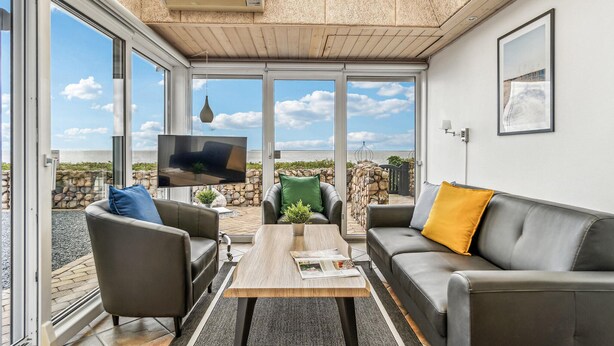Ein modernes Wohnzimmer mit großem Fernseher, bequemen Sitzgelegenheiten und Meerblick.