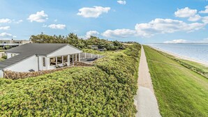 Ein Küsteneigentum mit einem gepflasterten Weg, der zum Strand führt, umgeben von üppiger Vegetation und einem modernen Haus mit großen Fenstern.