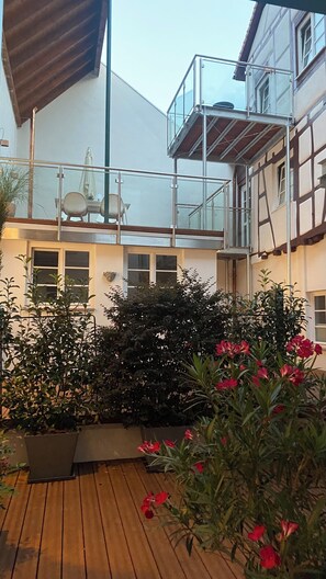 Un bâtiment doté d’une terrasse en bois, d’une balustrade en verre et d’un escalier en métal.