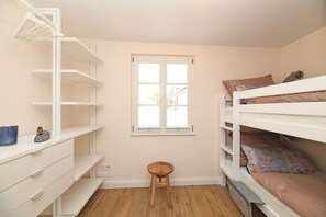 A bedroom with a bunk bed, a desk with drawers, a stool, and a window.