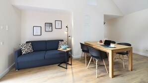 A modern living room with a dark blue sofa, a wooden dining table with four chairs, and a floor lamp. - Vacation apartment "Odenwald" with 2 bedrooms | The crooked house (Heppenheim (Bergstraße))