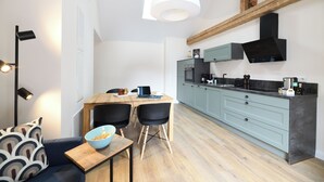 A modern kitchen with a dining area, featuring a wooden table, two black chairs, and a bowl of snacks on a small table. - Vacation apartment "Odenwald" with 2 bedrooms | The crooked house (Heppenheim (Bergstraße))