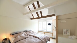 A bedroom with a bed, a bedside table with a lamp, a window, and a wall-mounted towel rack. - Vacation apartment "Odenwald" with 2 bedrooms | The crooked house (Heppenheim (Bergstraße))