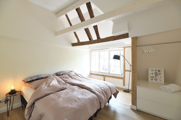 A bedroom with a bed, a bedside table with a lamp, a window, and a wall-mounted towel rack.