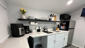 Una cocina moderna con armarios blancos, una cafetera negra, un hervidor y un microondas.