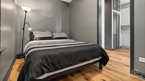 A modern bedroom with a bed, a floor lamp, and a view into the kitchen. - REMODELED Splendid Flat in Bucktown +Back Porch, Ranked GUEST FAVORITE! Pets OK! (Chicago)