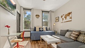 A compact living space with a bed, a sofa, a dining table, and a chair. There are two windows providing natural light and a view of the outdoors. - REMODELED Splendid Flat in Bucktown +Back Porch, Ranked GUEST FAVORITE! Pets OK! (Chicago)