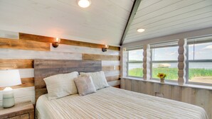 Un dormitorio con cabecera de madera, cama con ropa de cama a rayas, mesita de noche con lámpara y ventana con vistas al exterior.