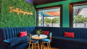 Un coin salon accueillant avec un canapé bleu foncé, deux fauteuils et une petite table sur laquelle est posée une plante. Un néon mural affiche l’inscription : « J’aime vraiment votre endroit. »