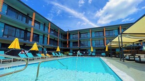 Un espace piscine d’hôtel doté de plusieurs niveaux de balcons, de parasols jaunes et de chaises longues.