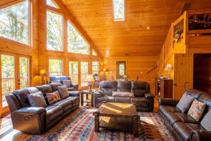 A spacious living room with leather sofas, a coffee table, and large windows offering views of the outdoors.