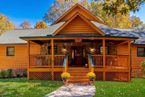 A log cabin with a stone foundation, a front porch with a railing, and a sign above the door.