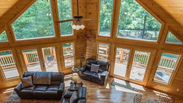 A spacious loft-style room with large windows, a ceiling fan, and a fireplace. - ALPINE RIVER ESCAPE - SECLUDED RIVERFRONT CABIN (Sautee Nacoochee)