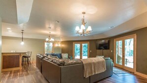 A spacious living room with a large sectional sofa, a dining area with a wooden table and chairs, and a kitchen area with a countertop and sink. - ALPINE RIVER ESCAPE - SECLUDED RIVERFRONT CABIN (Sautee Nacoochee)