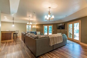 A spacious living room with a large sectional sofa, a dining area with a wooden table and chairs, and a kitchen area with a countertop and sink.