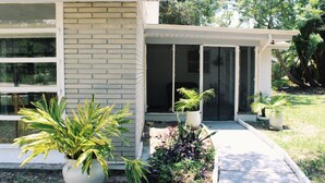 Een modern huis met een overdekte veranda, grote ramen en een tuin met potplanten.