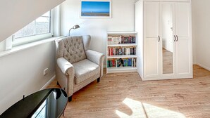 Een kamer met een raam, een stoel, een boekenkast en een garderobe.