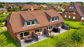 Een huis met twee verdiepingen, een betegeld dak, een terras met een tafel en stoelen, en een omheind gazon.