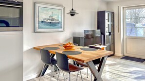 Een eetruimte met een houten tafel, vier stoelen, een fruitschaal, een televisie en een lijst aan de muur.