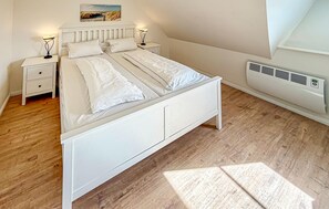 Un dormitorio con una cama blanca, dos mesitas de noche con lámparas, un aire acondicionado de pared y un cuadro sobre la cama.