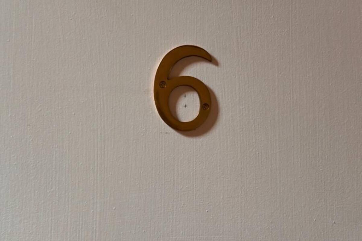 Una pared blanca con un letrero de latón con el número 6.