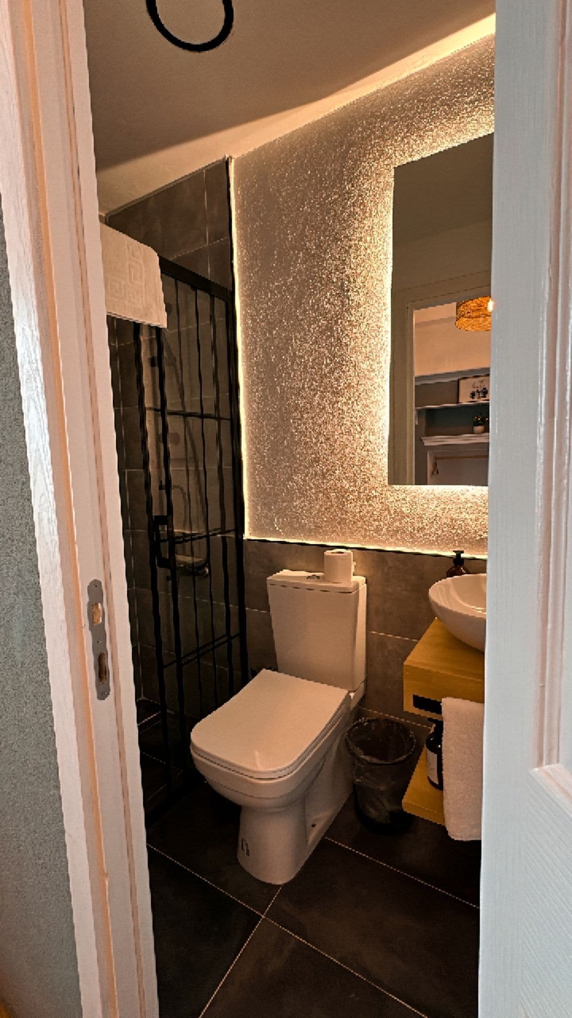 A bathroom with a toilet, a shower enclosure, a sink, and a mirror.