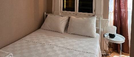 Ein Schlafzimmer mit einem großen Bett, weißen Bettwäsche, einem kleinen Nachttisch und einem Fenster mit Vorhängen.