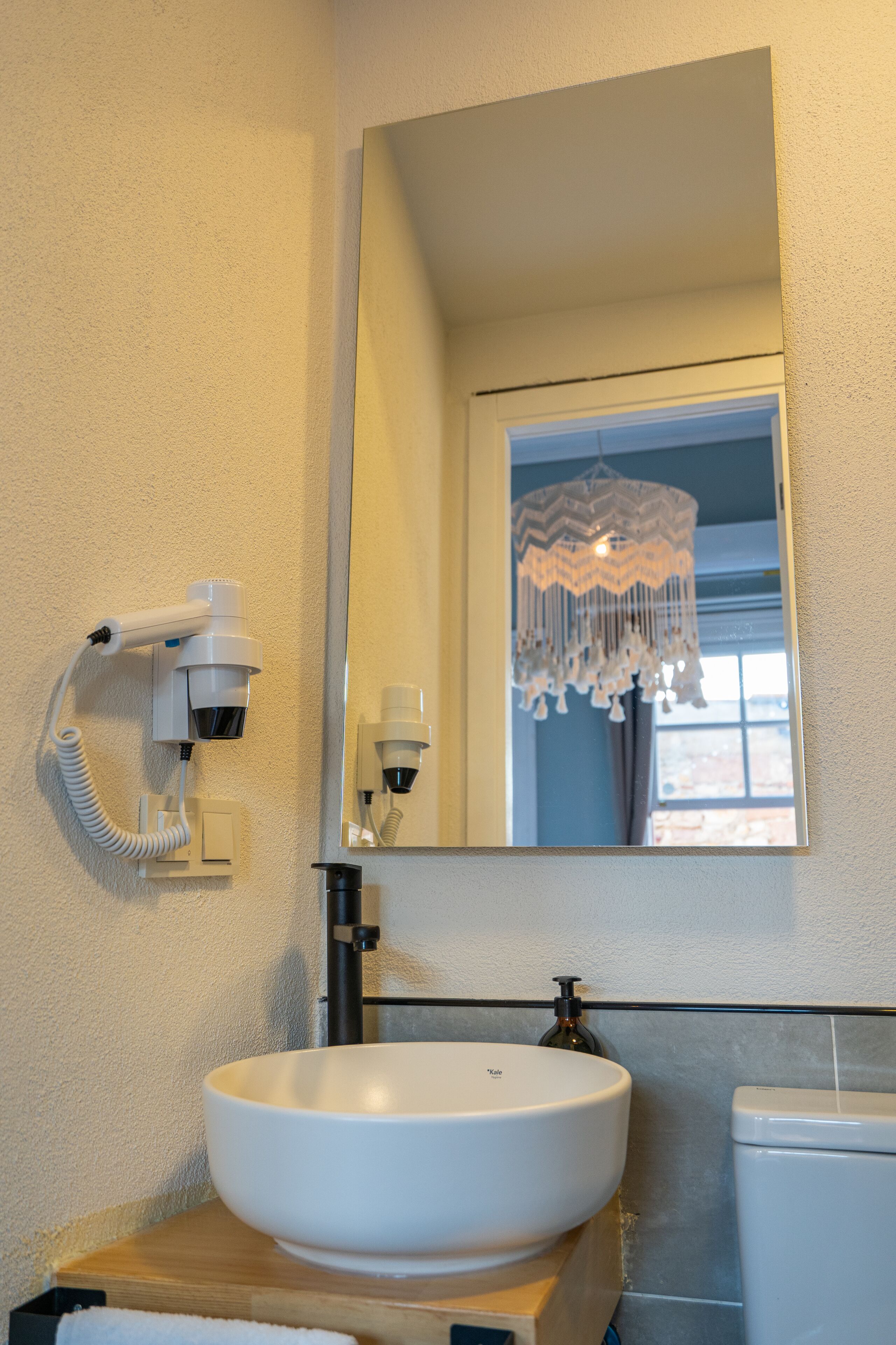 Ein Badezimmer mit einem weißen Waschbecken, einem Spiegel, einem Föhn und einer Chandelüster.