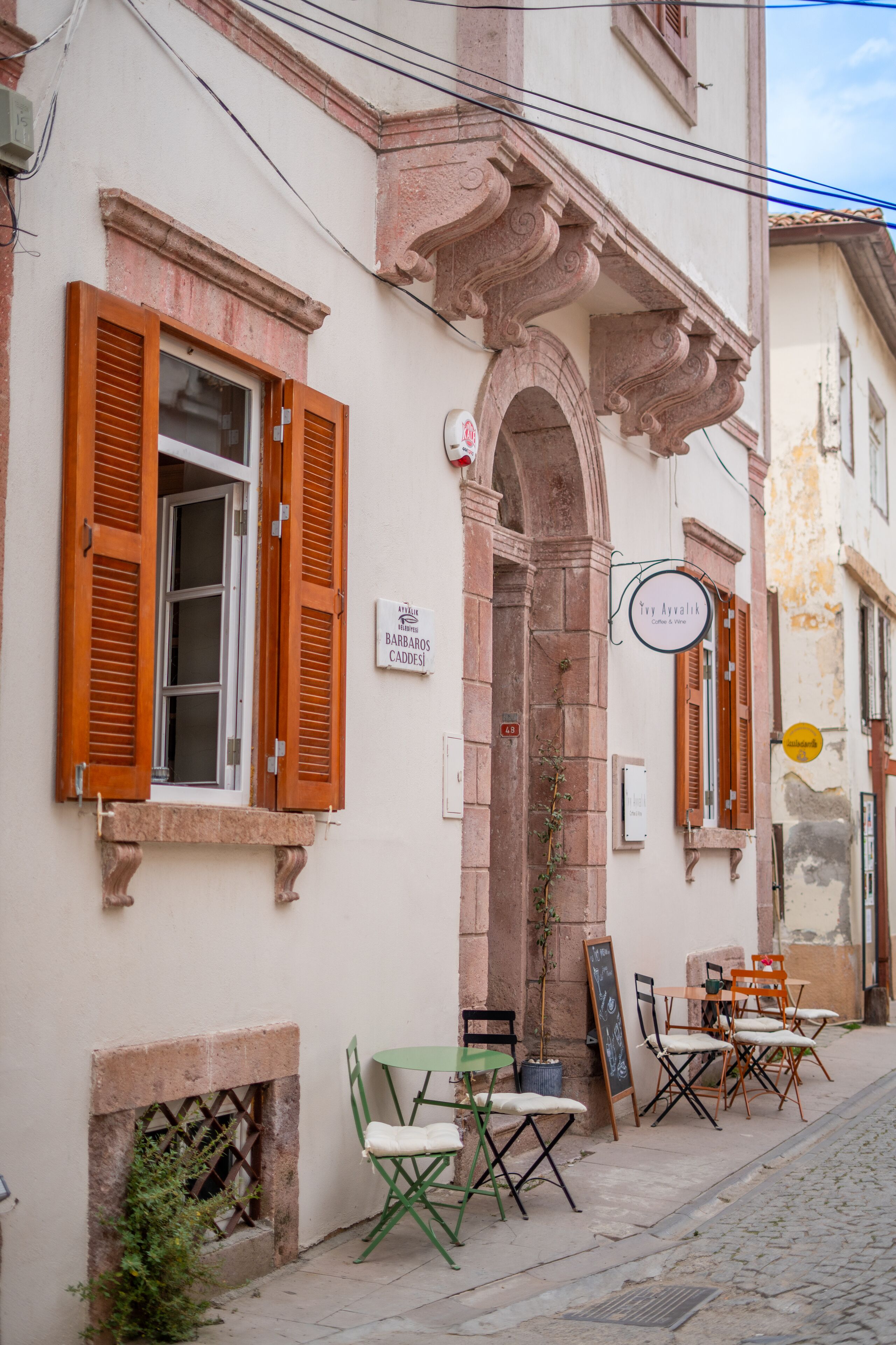 A street-side cafe with outdoor seating, a signboard, and a small entrance.