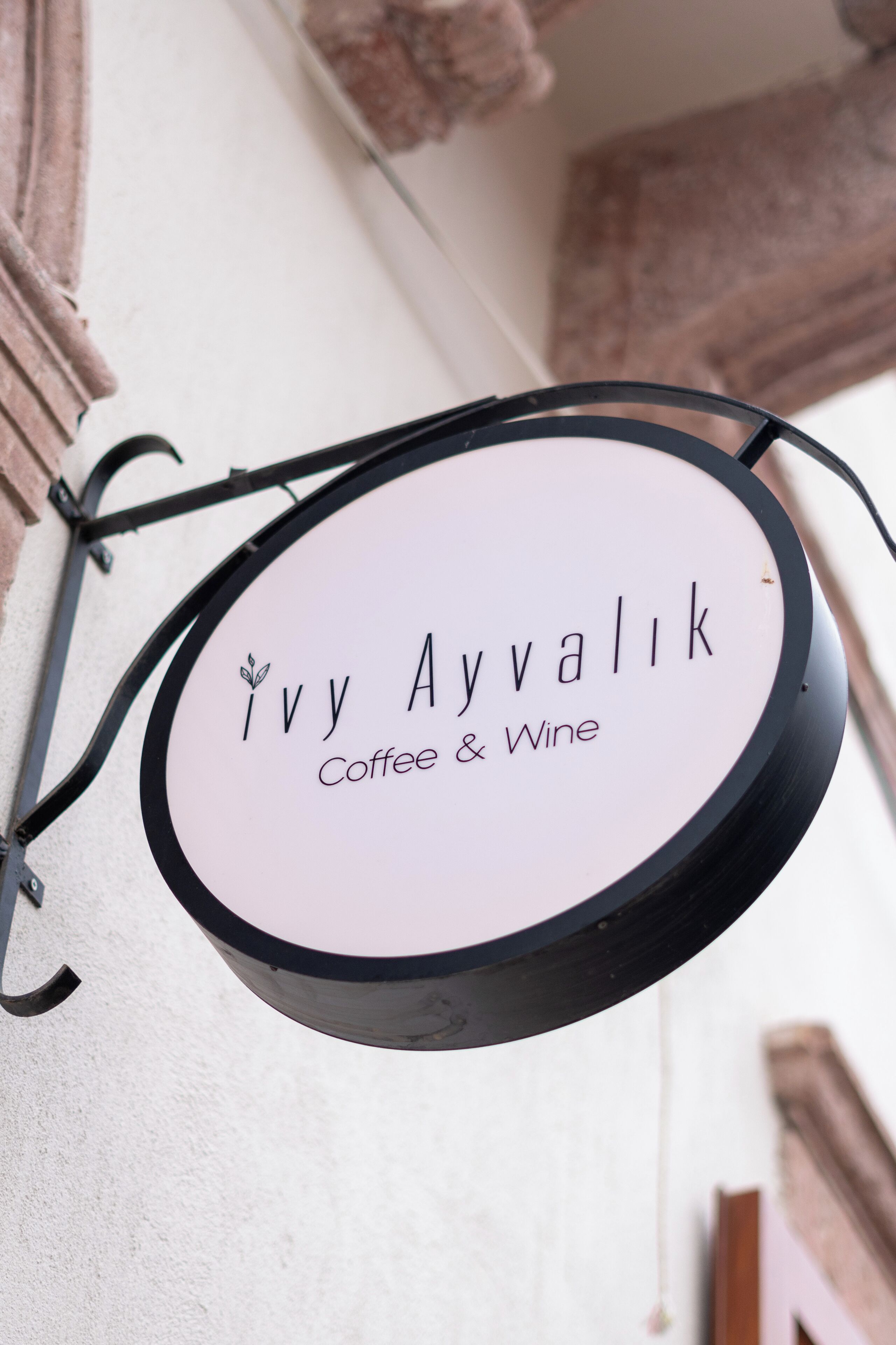 A circular sign with the text "Ivy Ayvalik Coffee & Wine" hanging from a metal bracket.