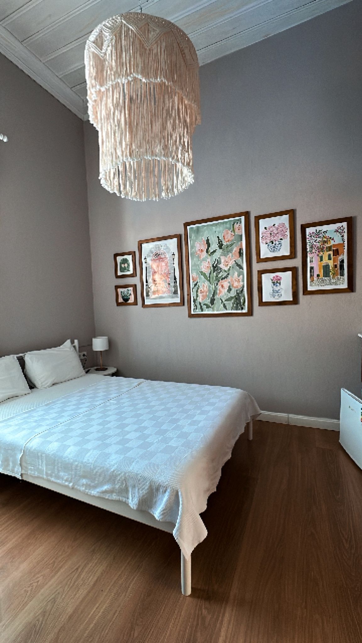Une chambre à coucher comprenant un lit, une table de chevet, une lampe et un mur orné de tableaux encadrés.