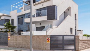Un moderno edificio residencial de varios pisos con balcones, entrada protegida y cielo despejado.