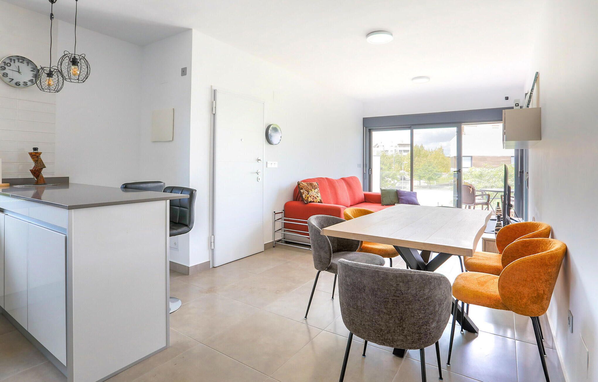 Eine moderne Küche mit Kochinsel, einem Essbereich mit Tisch und Stühlen, einem roten Sofa und einem großen Fenster mit Blick ins Freie.