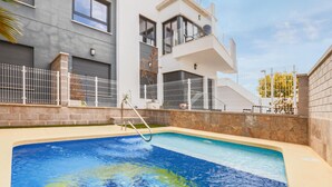 Un edificio residencial moderno con piscina, cercas blancas y una escalera que lleva a un balcón.