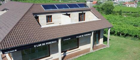 Um edifício com telhado inclinado, painéis solares e uma placa com a inscrição 'O LAR DE PEREIRAS'.