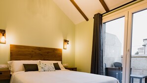 A hotel room with a wooden headboard, a large bed with white bedding, two bedside lamps, and a view of the outside through a glass door.